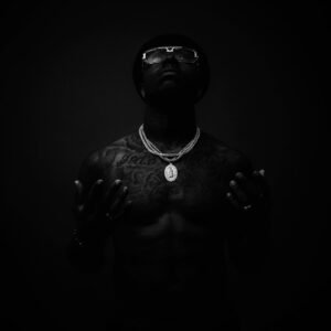 topless man with tattoos wearing eyeglasses and pendant necklace looking pu